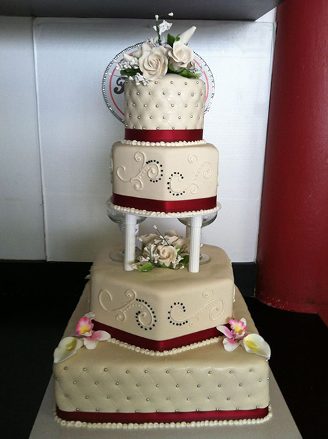 Four layer white wedding cake with red ribbon, pearls, and flower accents.